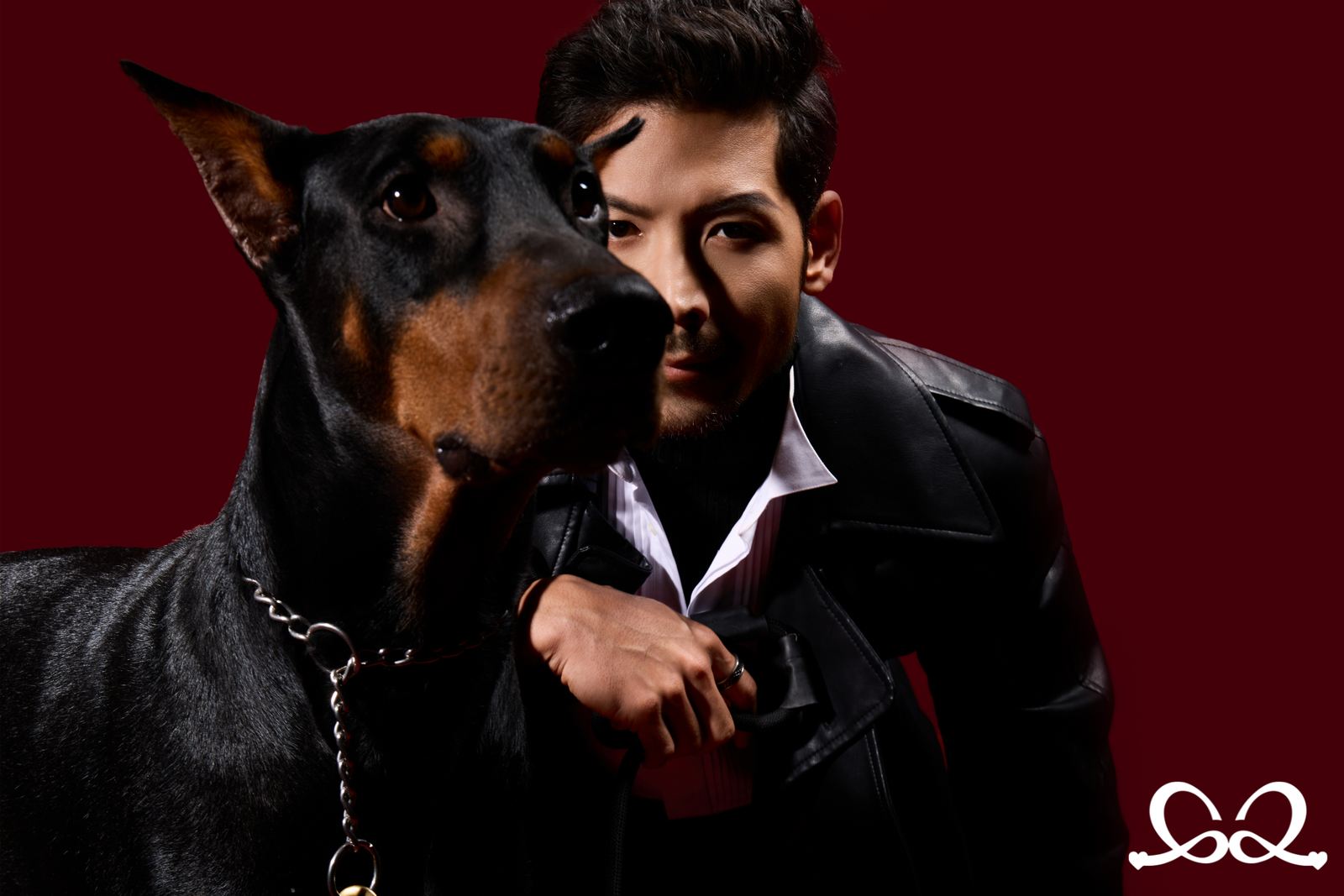 A studio portrait — a man in a leather coat beside his Doberman on a deep red ground