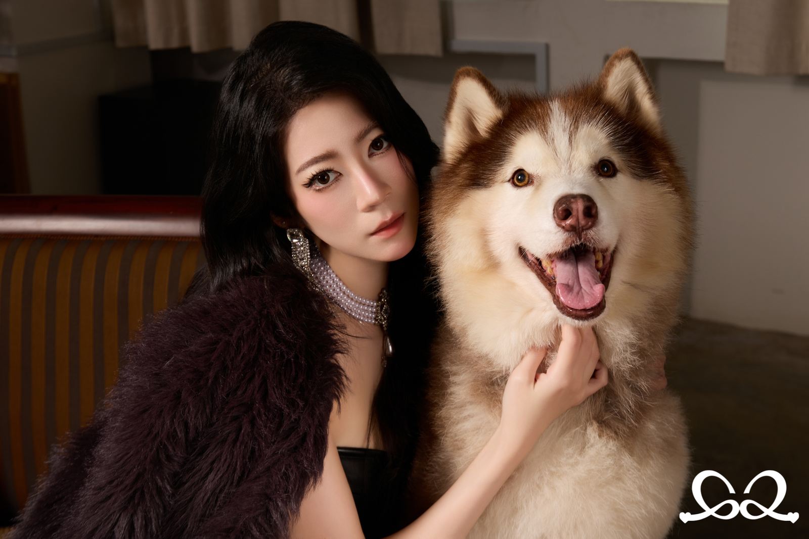 A portrait at home — a woman resting her hand on her red-and-white Alaskan Malamute