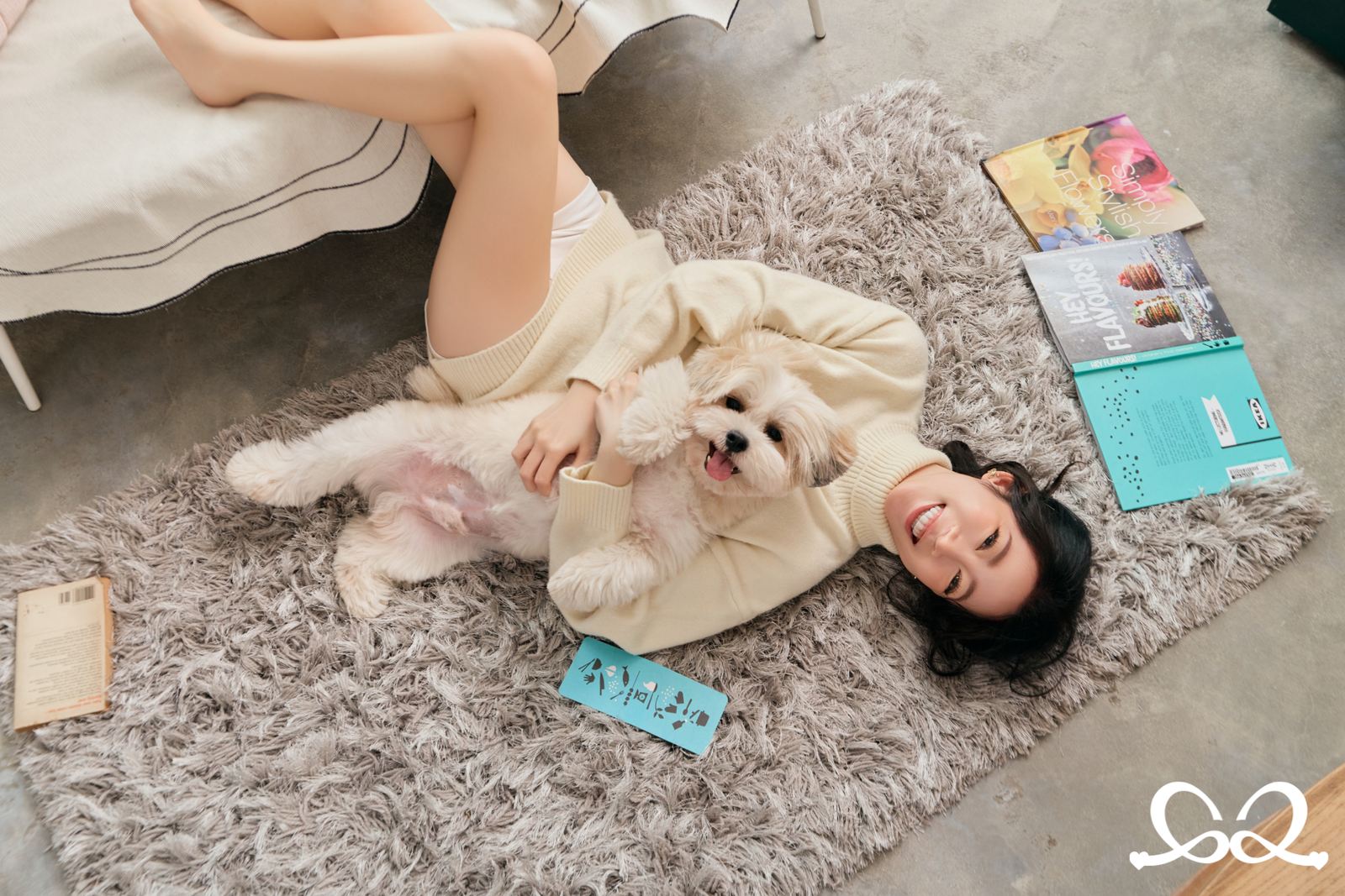 An everyday moment — a woman lying on a rug at home, laughing, holding her small dog